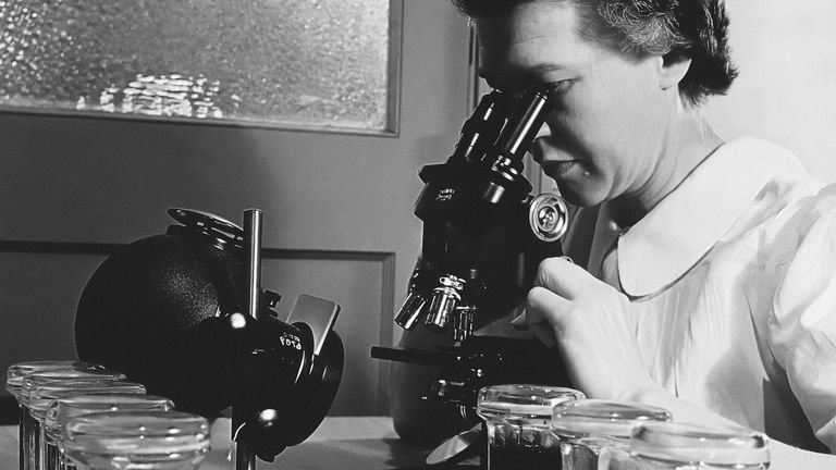 Pesquisadora utilizando microscópio em laboratório para avaliação microbiológica